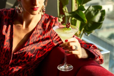 Woman in a red leopard print dress holding a martini glass garnished with cucumber ribbons in a bar.