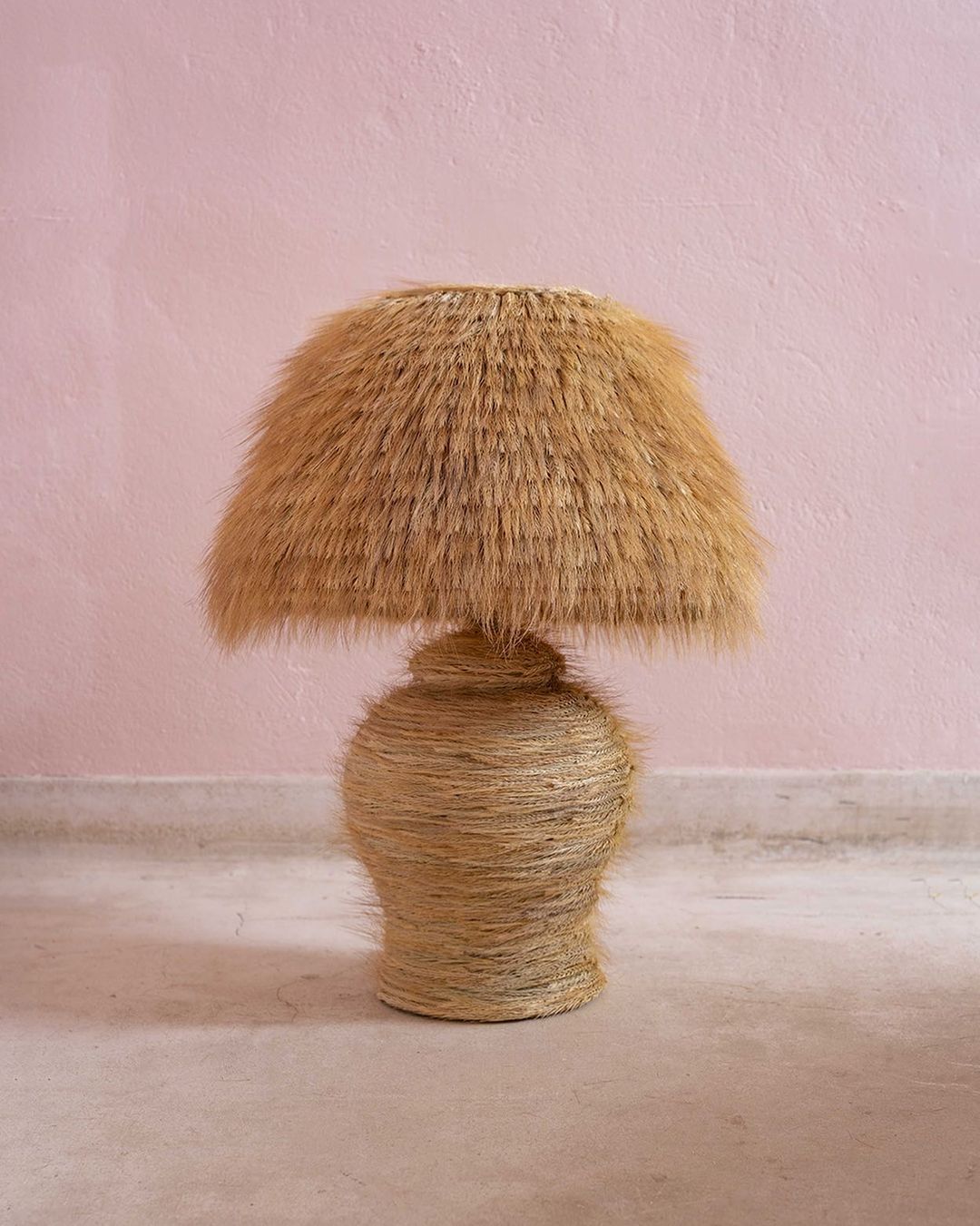 Straw table lamp in a neutral tone against a light pink wall, showcasing rustic textures and minimalist home decor.