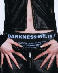 Close-up of a person in a black leather jacket and pants adjusting the waistband with long manicured nails