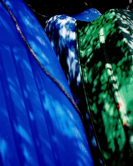 Close-up of blue, white, and green boats stacked vertically, showcasing colorful hulls and shadows under bright lighting conditions.
