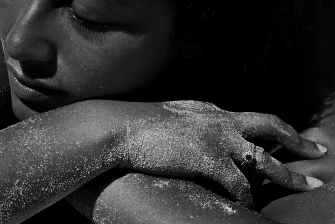 Extreme close-up monochrome photograph of a person resting their head on an arm covered in sand.
