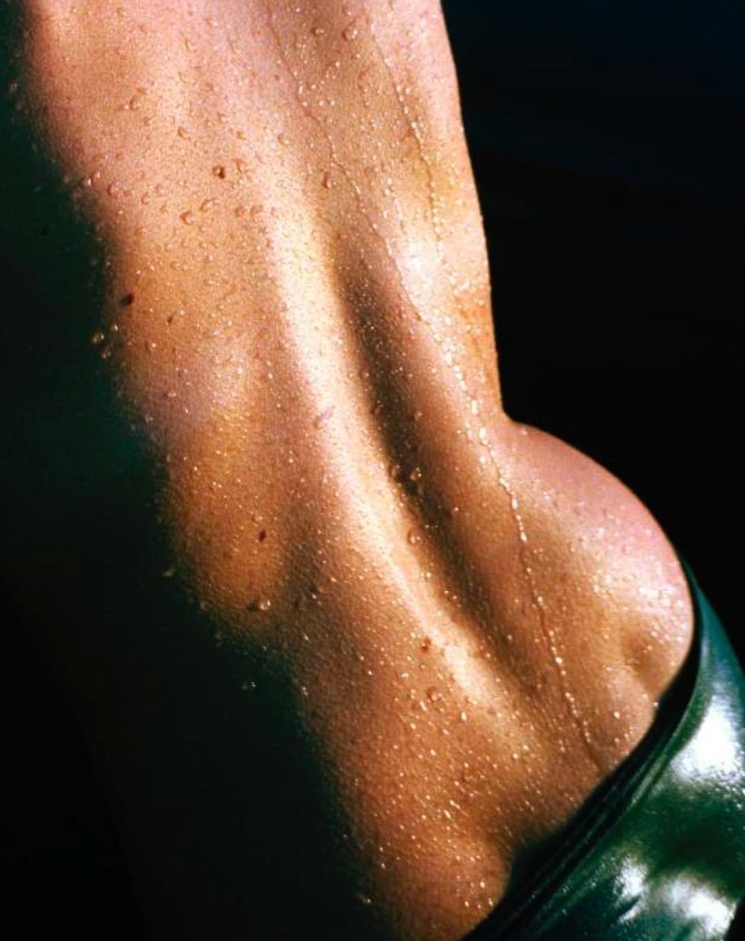 Close-up of a woman's wet back and shoulder, showcasing muscle definition and glistening skin against a dark background.