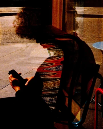 Silhouetted person seated at a table holding a smartphone with multiple exposure reflections and patterns.