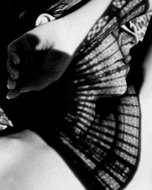 Monochrome close-up of a person's face and hand, overlaid with a patterned shadow creating a striking contrast of light and dark.