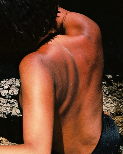 Woman's back with tan lines, skin texture, and water droplets, captured in a natural outdoor setting with a shallow depth of field.