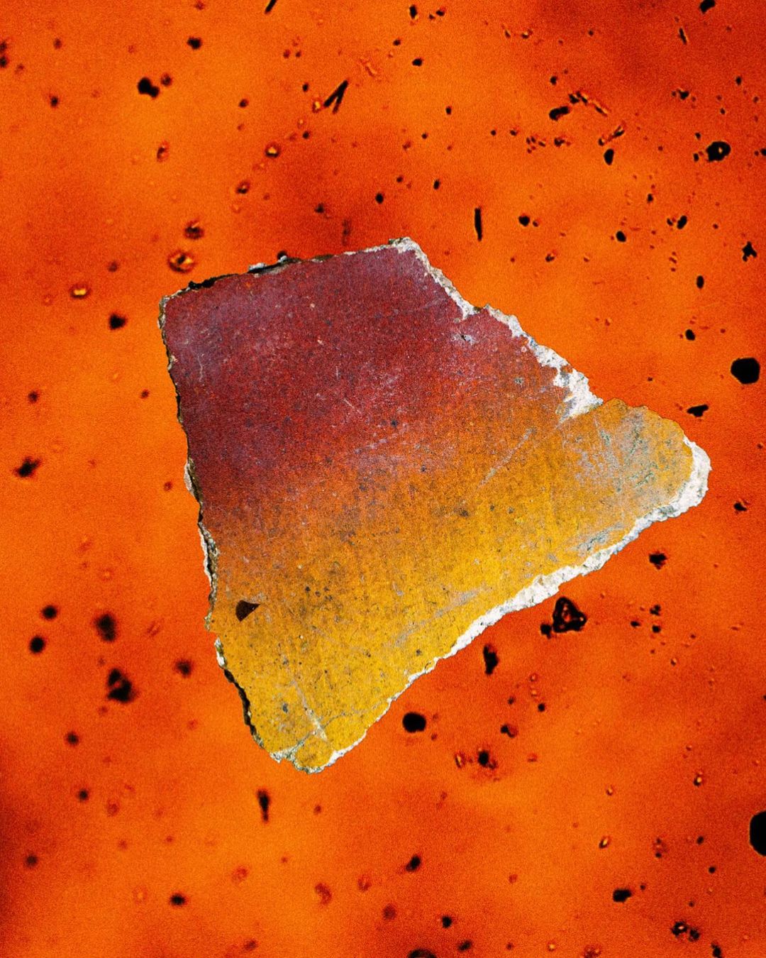 Abstract image featuring a color gradient paper scrap with red and yellow hues against an orange background with dark speckles.
