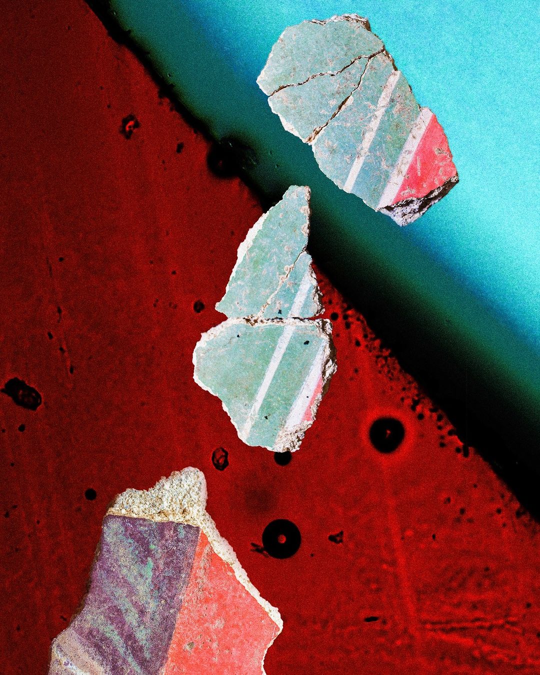 Close-up shot of colorful painted wall fragments in red, turquoise, green, and purple, displaying geometric patterns and rough textures.