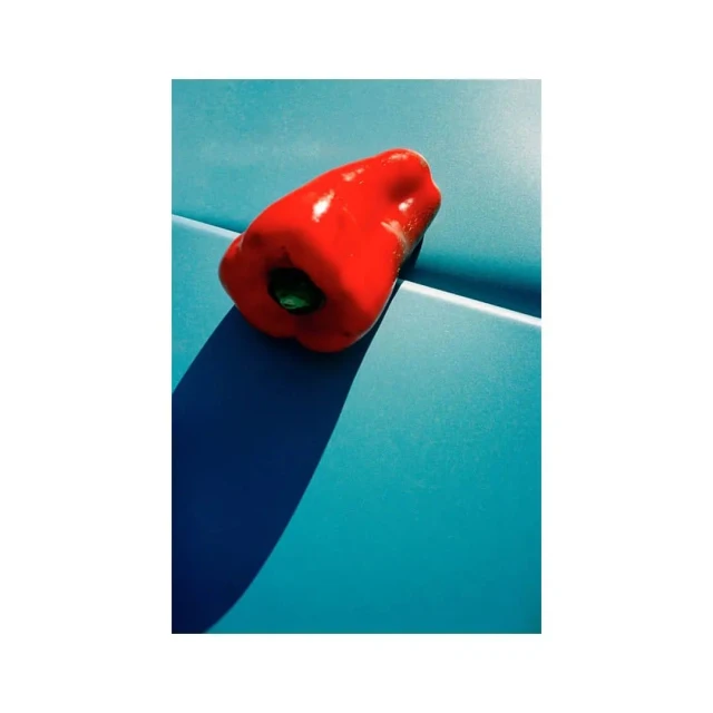 Striking still life of a shiny red bell pepper on a glossy turquoise surface, showcasing bold color contrast and modern composition.