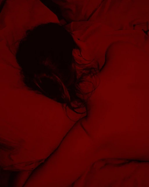Close-up photo of a woman lying on a red surface, her dark hair visible, in a photograph using a red color grade and shallow depth of field.