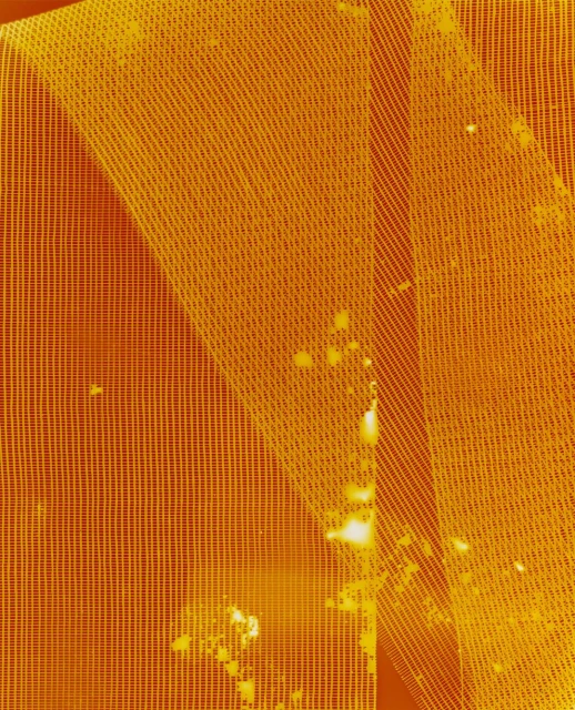 Close-up abstract view of mesh netting material with spots of discoloration, textured surface with a yellow-orange color cast. 