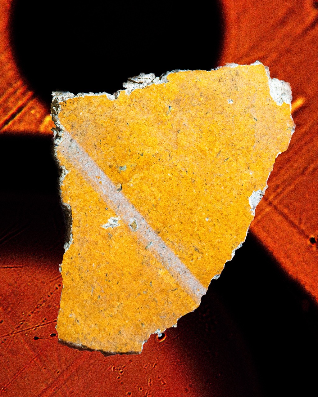 Close-up of rough yellow and white material fragment with a geometric, diagonal white stripe, against a dark background.