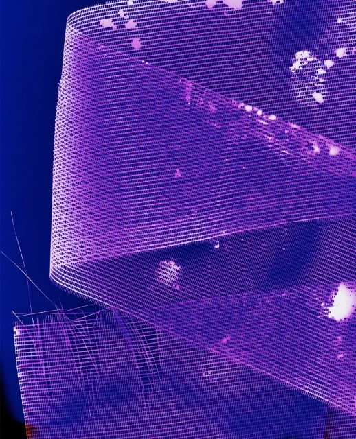 Macro shot of purple wire mesh ribbon abstractly arranged against a dark blue background, creating a textured and colorful pattern.