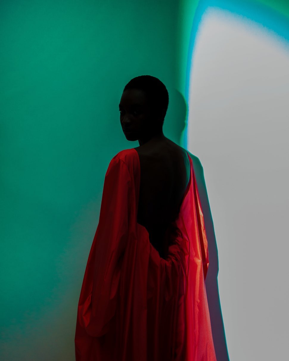 Back view of a Black woman wearing a red open back dress. The background is a blue and white gradient wall. Studio lighting.