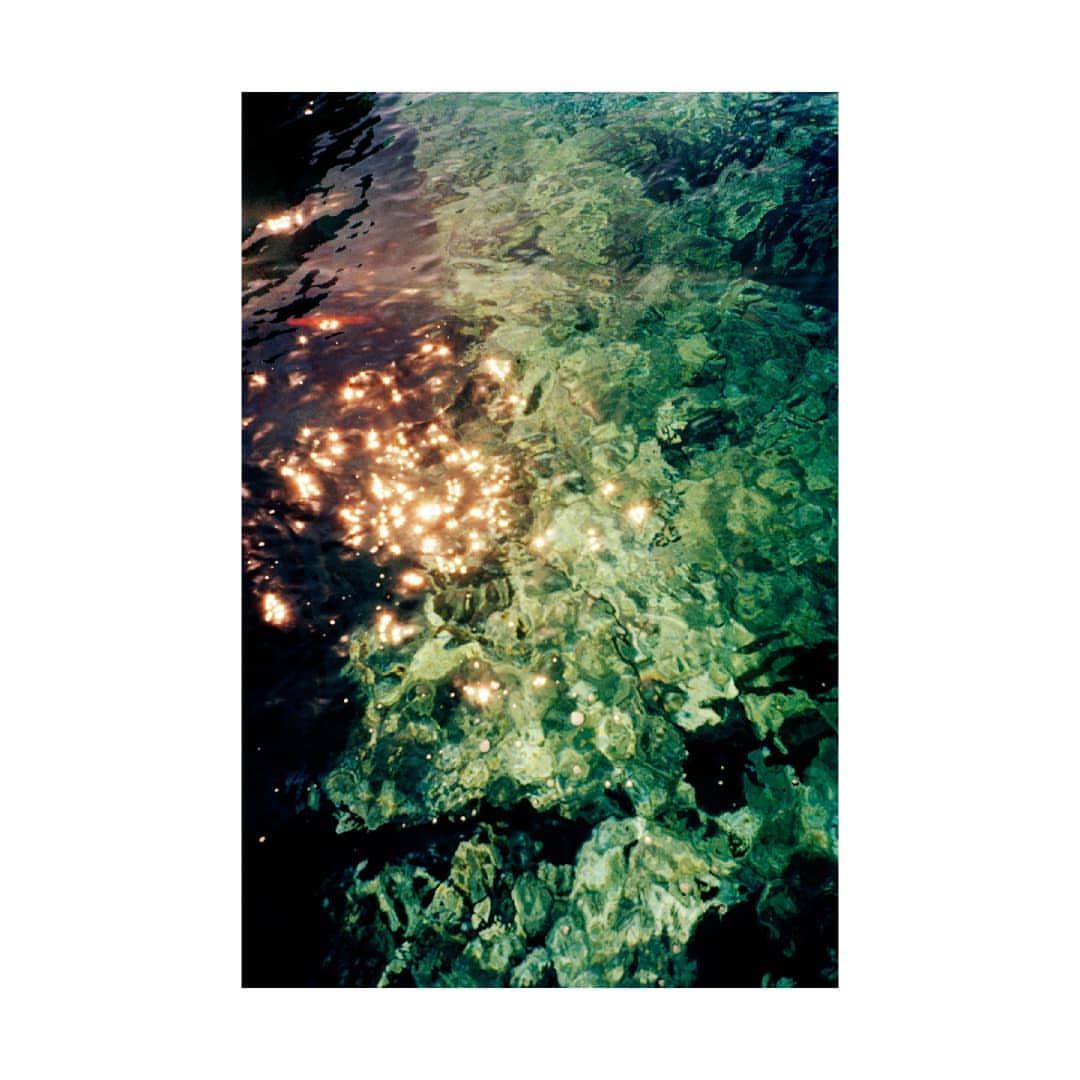 Underwater shot of shimmering turquoise water with rocks, capturing the interplay of light and shadow in a tranquil seascape.