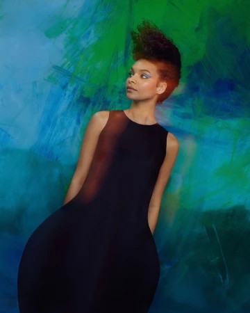 Woman in a black dress with dramatic swept-up hair posing against a vibrant blue and green painted backdrop