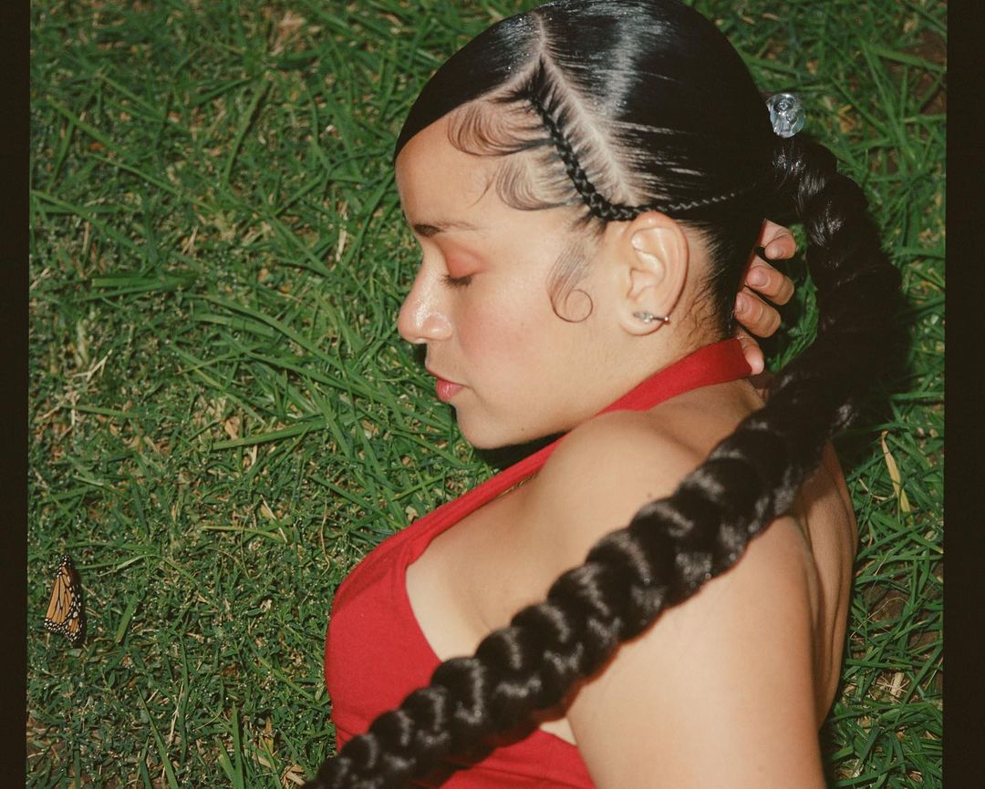 Profile of a young adult female laying in the grass with a braid. She's wearing a red halter top and has braided hair.