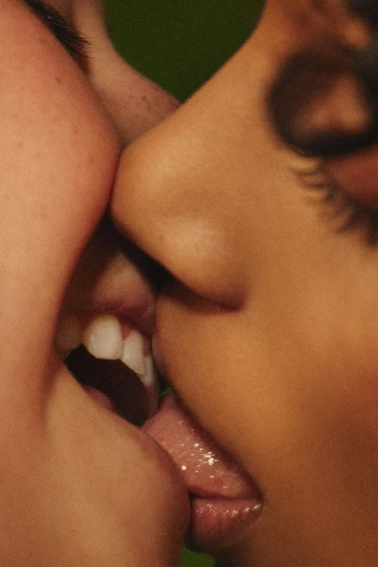 Close-up studio portrait of two people kissing with tongues touching, soft studio lighting, and a green background, intimate and sensual.