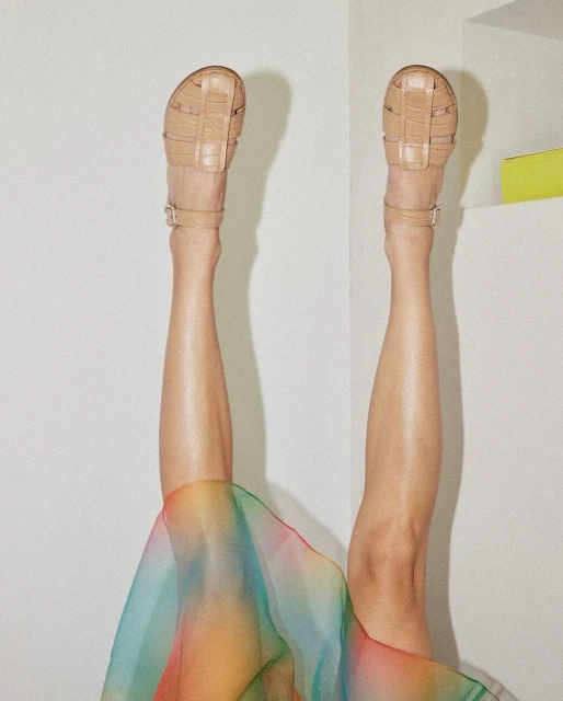 Upside down view of woman's legs wearing beige sandals with a colorful sheer fabric against a white wall and yellow accent.
