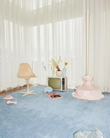 Retro-inspired interior featuring a blue carpet, vintage television, beige chair, pink sculptural form, and sheer white curtains.