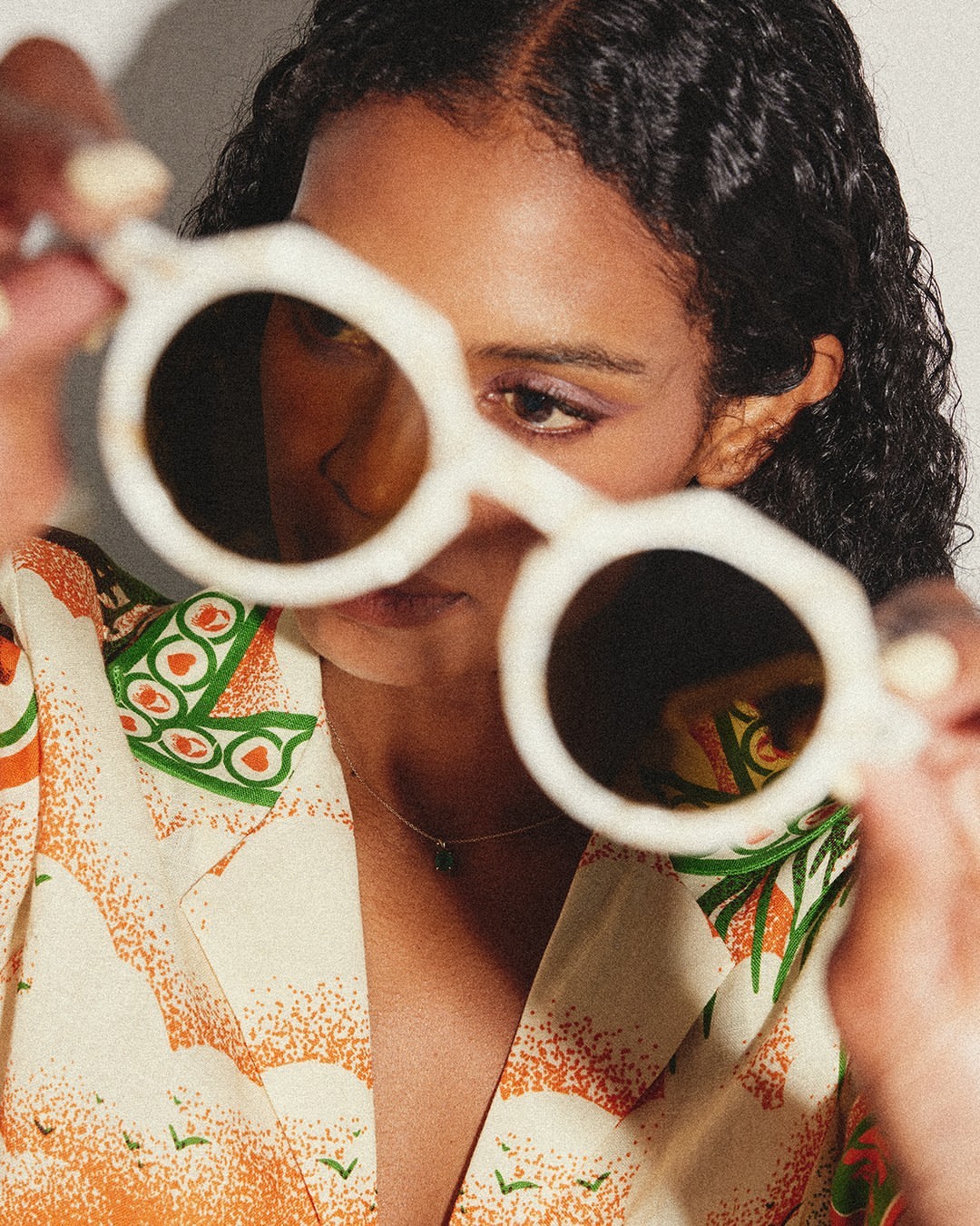 Close-up portrait of a woman holding large white-framed round sunglasses up to the camera by Maria Del Rio