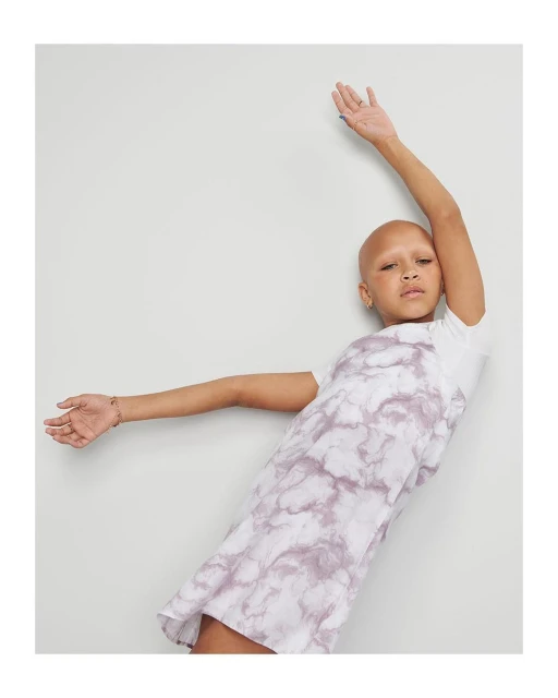Woman in a tie-dye dress poses with arms outstretched against a neutral background in a fashion shoot with natural light.