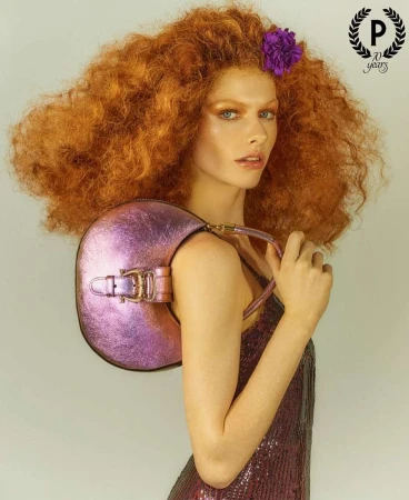 Red-haired female model holding a metallic purple handbag in profile shot by Mariano Vivanco.