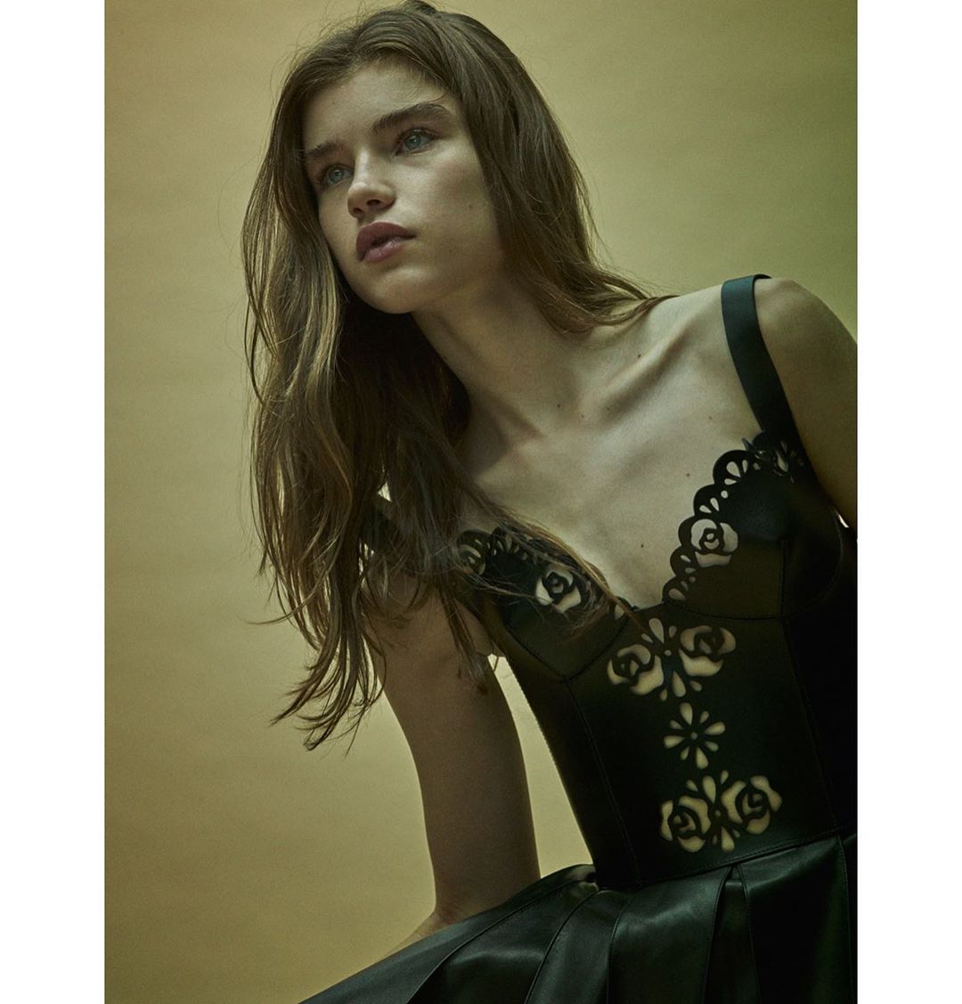 Woman in elegant black dress with floral cut-out bodice in a high-fashion studio portrait with diffused lighting and neutral background.