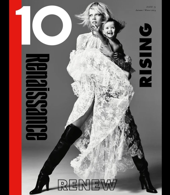 Fashion editorial shot of a fair-skinned adult female model in a laced dress holding an infant on a grey background with magazine text.