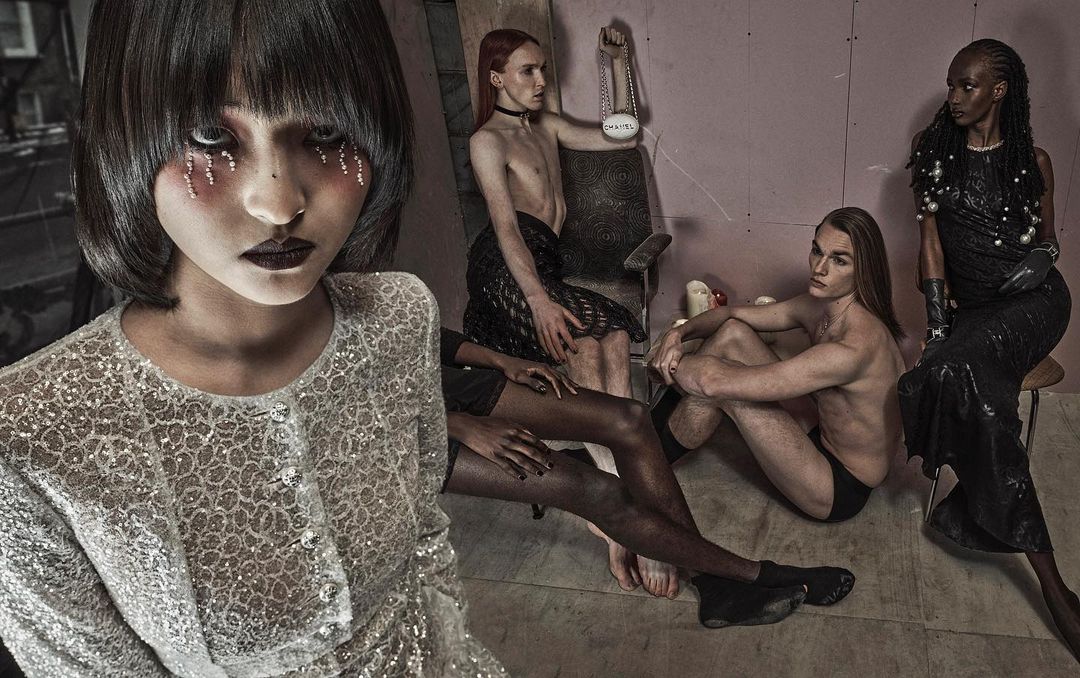 Artistic group portrait of five people in a staged studio setting with textured walls, bold makeup, and dramatic dark fashion.