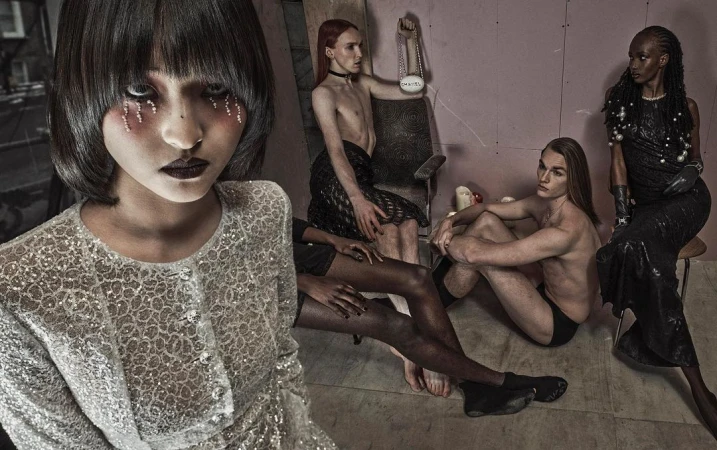 Artistic group portrait of five people in a staged studio setting with textured walls, bold makeup, and dramatic dark fashion.