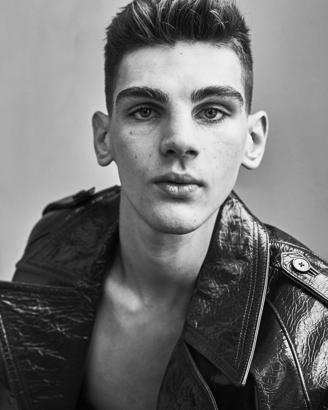 Close-up portrait of a young man wearing a textured leather jacket against a neutral studio background