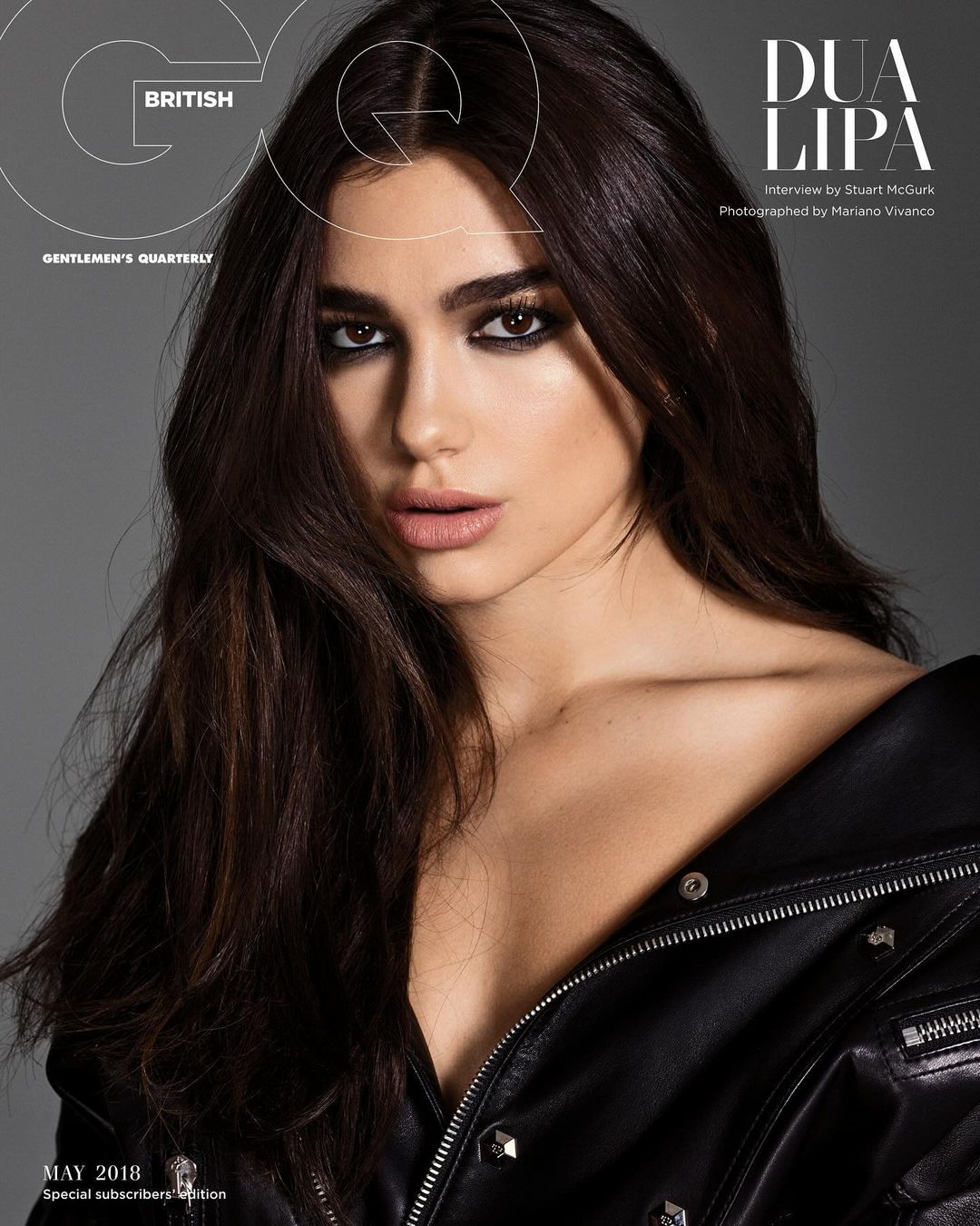 British GQ cover featuring Dua Lipa in a low-cut black leather jacket, sultry makeup, and dark hair on a grey backdrop. Fashion magazine cover.