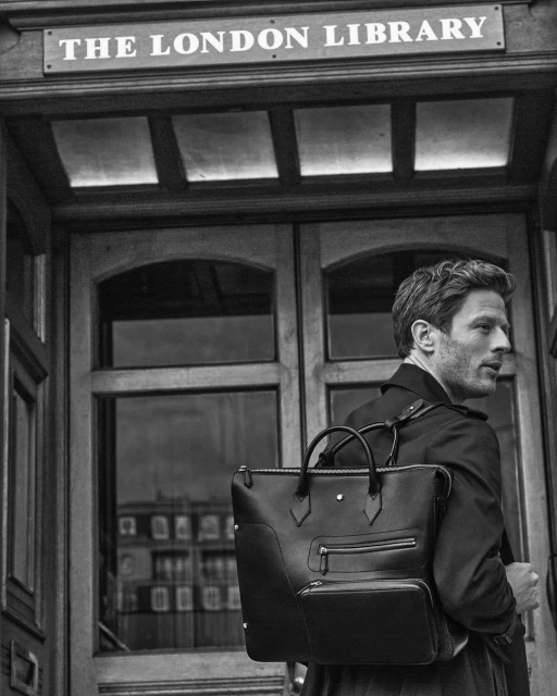 A man with a briefcase stands outside The London Library, captured in black and white with natural lighting and a neutral expression.