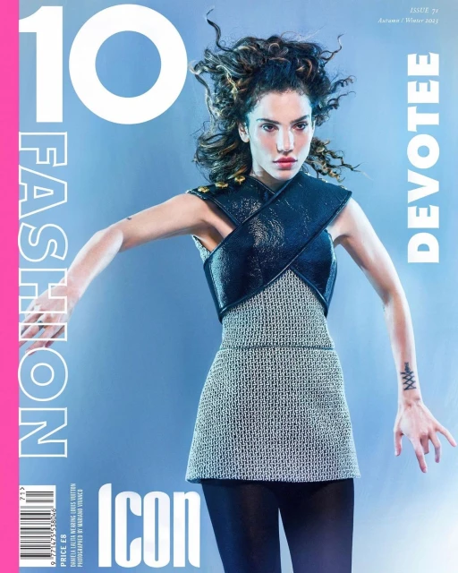 Fashion magazine cover featuring a woman with curly hair wearing a structured outfit against a gradient blue background with bright pink text.