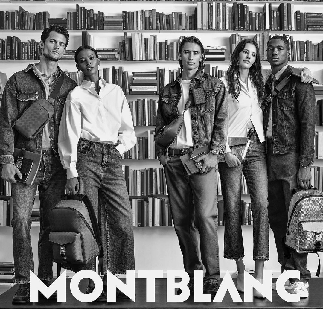 Montblanc advertisement featuring five diverse models in denim and white shirts standing in front of a bookshelf in a monochrome filter.