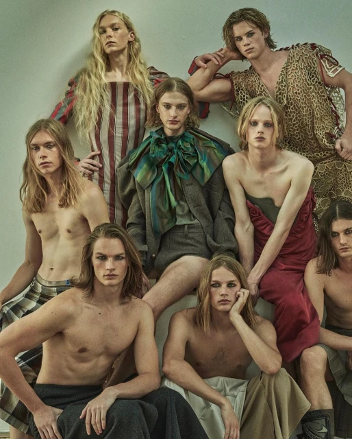 A diverse group of androgynous-looking male fashion models with long hair in various poses and attire in a studio setting.