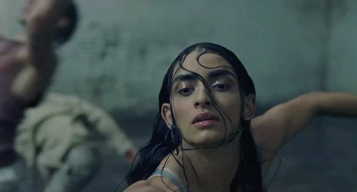 Dramatic close-up of androgynous person with wet dark hair against a blurred background, capturing a moody and intense atmosphere.