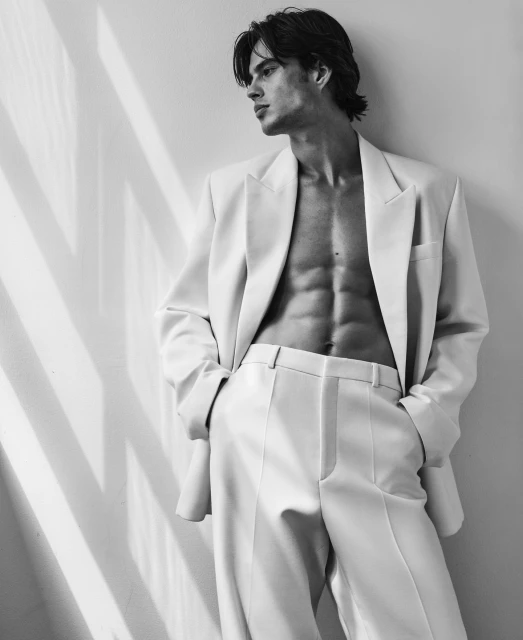 Black and white portrait of a male model wearing a suit with no shirt, showcasing abs and looking off to the side with shadows.