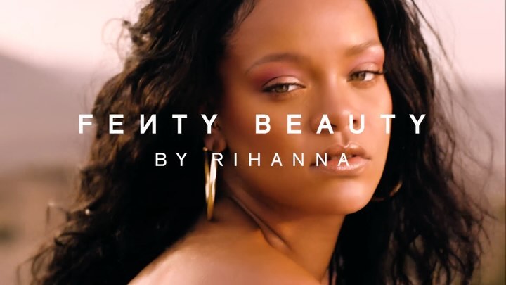 Close-up portrait of Rihanna for Fenty Beauty ad, featuring makeup details, gold hoop earrings, and a blurred background.