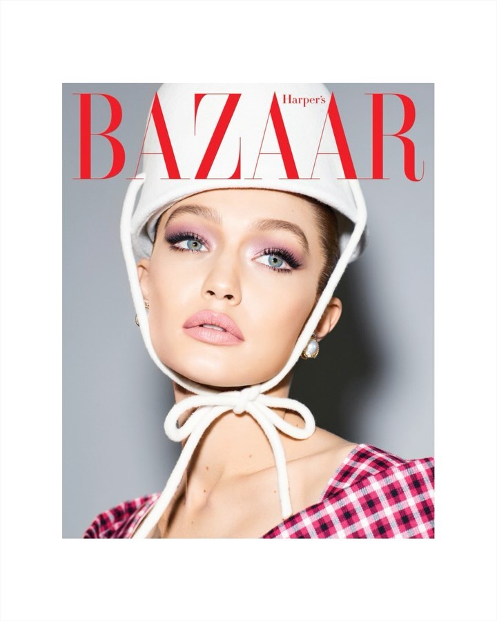Magazine cover featuring a close-up of model Gigi Hadid wearing a white hat and pink plaid top, against a grey background.