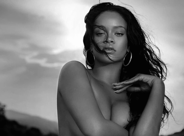 Monochrome portrait of Rihanna with dark flowing hair and large hoop earrings against an outdoor sky background by Mariano Vivanco.