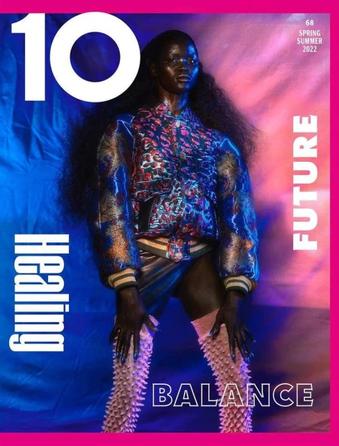 Magazine cover featuring a dark-skinned female model in a patterned jacket and unique boots against a vibrant pink and blue background.