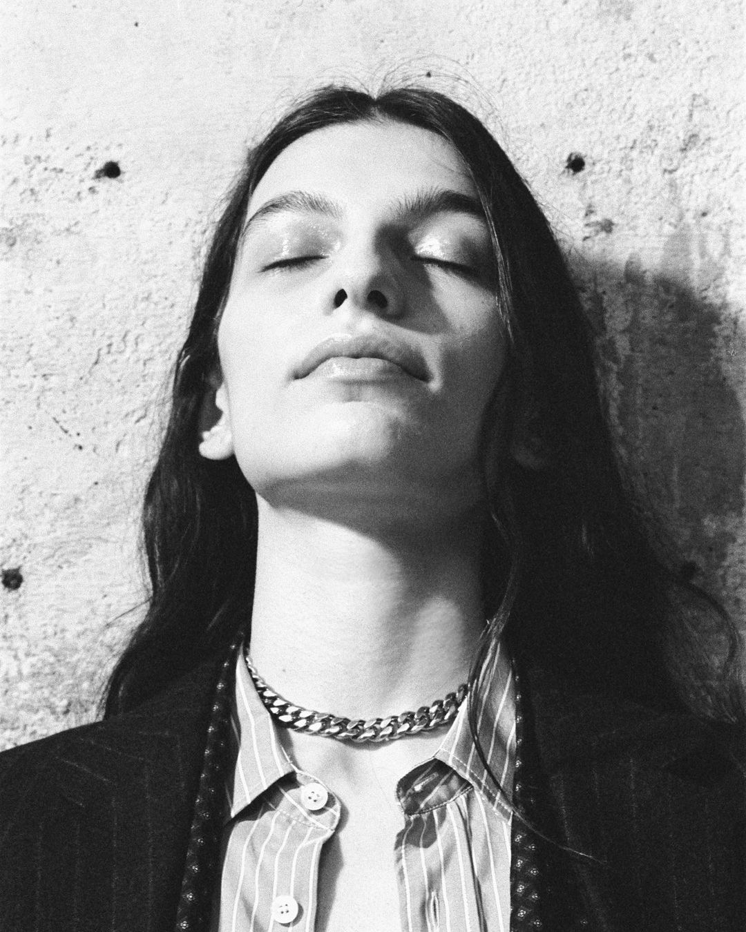 Close-up monochrome portrait of a woman with eyes closed wearing a striped shirt and silver chain necklace