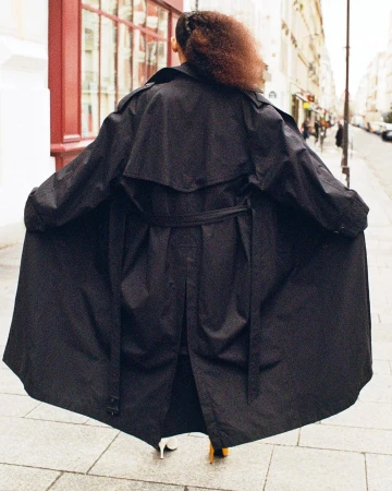 Model seen from behind wearing an oversized dark trench coat on a Paris street, captured by Marie Deteneuille.
