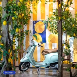 Light blue motor scooter parked in front of a yellow and white striped wall with lemon trees