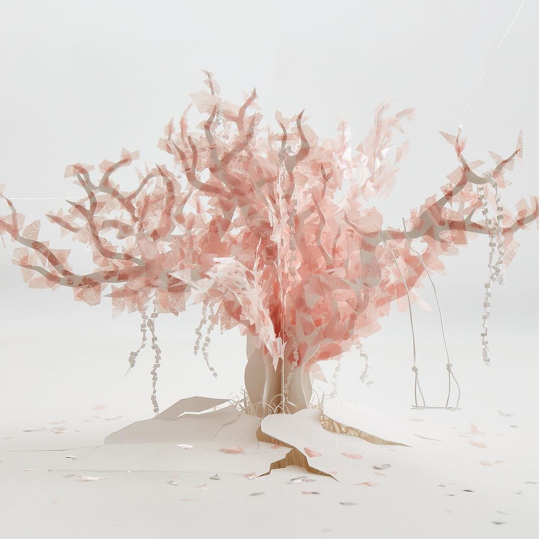 Artistic paper art of a pink tree with a swing, set against a white background in a studio for a whimsical, conceptual aesthetic.