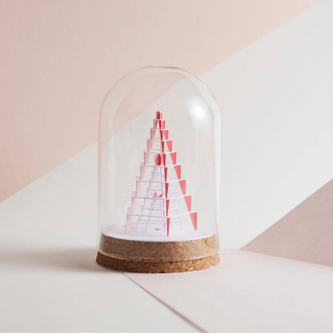 Paper Christmas tree under a glass cloche. A Christmas decoration on a geometric background of pink and white, studio lighting.