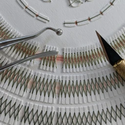 Close-up of intricate paper art and green thread stitching on white paper with metal sculpting tools and a craft knife