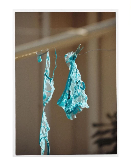 Two pieces of blue and white lace lingerie hang on a clothesline with clothespins in an indoor setting with neutral-colored walls.