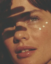 Close-up portrait of a woman with freckles and harsh directional shadows across her face by Marie Schmidt